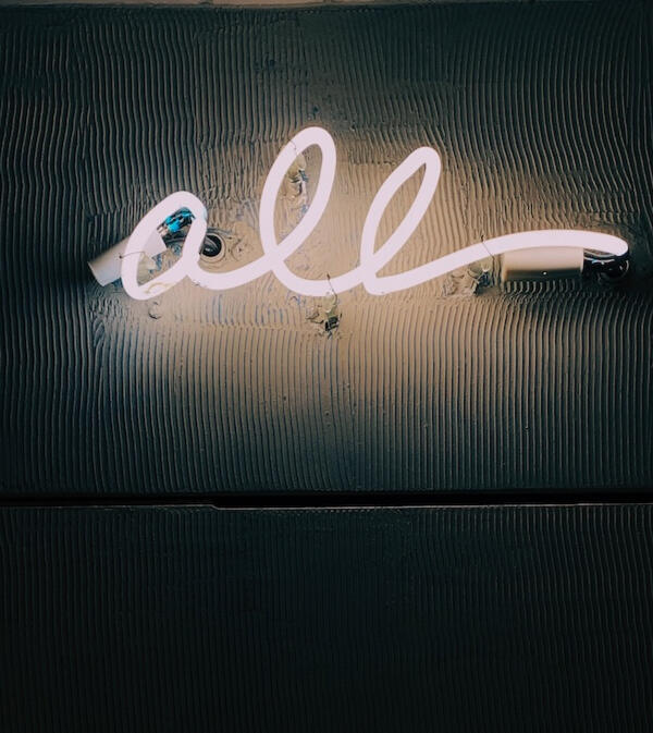 An einer Wand hängt ein Neonschriftzug, auf dem das englische Wort all steht.