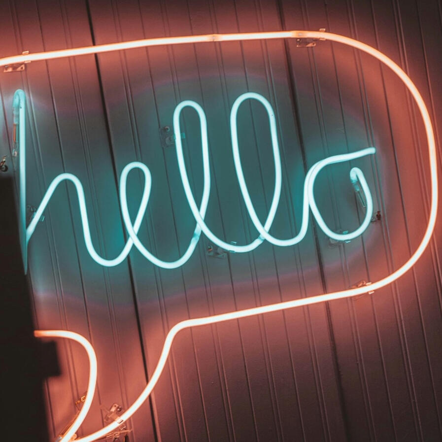 Eine Lichtinstallation hängt an einer Wand. Sie ist in der Form einer Sprechblase, in der "hello" steht.